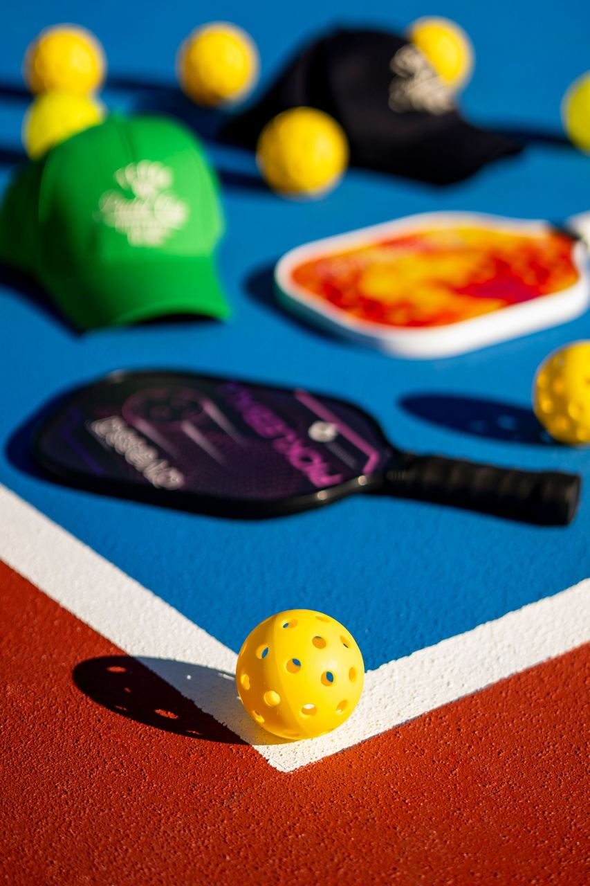 Pickleball paddles and yellow balls on an outdoor blue court, illustrative stock photograph